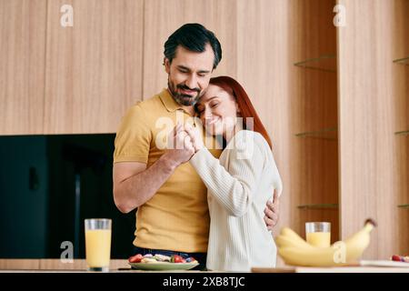 Une femme rousse et un homme barbu s'embrassent passionnément dans une cuisine moderne, mettant en valeur l'amour et la convivialité. Banque D'Images