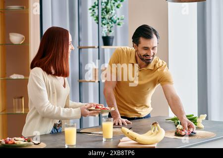 Une femme rousse et un homme barbu préparent la nourriture ensemble dans une cuisine moderne, mettant en valeur le travail d'équipe et l'unité. Banque D'Images