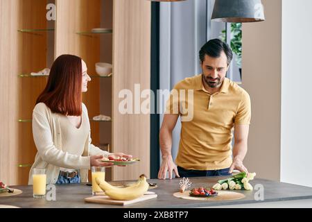 Une femme rousse et un homme barbu cuisinent ensemble dans une cuisine moderne, se liant à la préparation des aliments et au temps de qualité. Banque D'Images