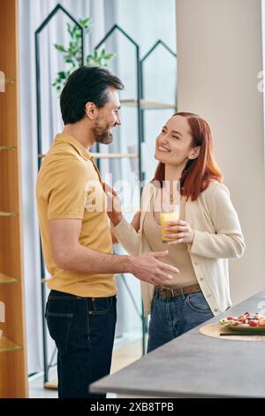 Un homme barbu et une femme rousse se sont engagés dans une conversation profonde tout en se tenant debout dans une cuisine moderne. Banque D'Images