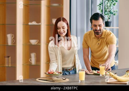 Une femme rousse et un homme barbu préparent les ingrédients et cuisinent ensemble dans une cuisine d'appartement moderne. Banque D'Images