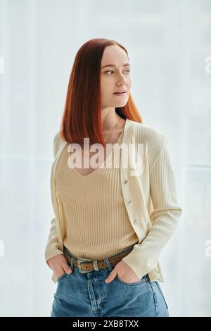 Une femme rousse en attente de temps de qualité dans un appartement moderne. La femme porte un Jean et un cardigan blanc. Banque D'Images