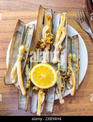 Palourdes grillées à l'espagnole, garnies d'ail et d'une tranche de citron, servies sur une table en bois. Banque D'Images