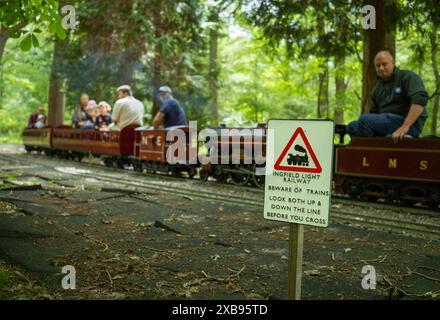 Un train à vapeur miniature à voie étroite transportant des passagers passe devant un panneau de chemin de fer et traverse les bois à Ingfield Manor School, Five Oaks, West sus Banque D'Images