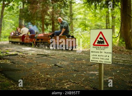 Un train à vapeur miniature à voie étroite transportant des passagers passe devant un panneau de chemin de fer et traverse les bois à Ingfield Manor School, Five Oaks, West sus Banque D'Images