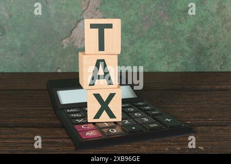 Pile de blocs de bois montrant la TAXE DE texte vert sur une calculatrice de bureau noire sur une table en bois. Fiscalité, évasion fiscale et comptabilité Banque D'Images