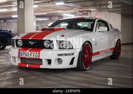 Impressionnante voiture de sport américaine garée dans un parking, il s’agit d’une Ford Mustang GT de cinquième génération, blanche avec des bandes rouges et des roues rouges. Banque D'Images