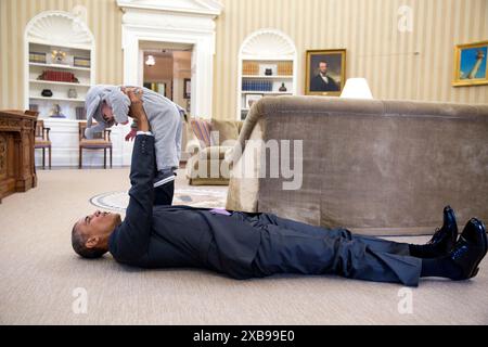 Le président Barack Obama tient Ella Harper Rhodes, fille de Ben Rhodes, conseiller adjoint à la sécurité nationale pour les communications stratégiques, alors qu'il est allongé sur le sol dans le bureau ovale - photographe officiel de la Maison Blanche Banque D'Images