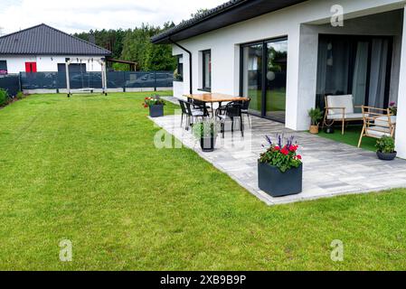 Diverses fleurs et herbes debout sur la terrasse dans un grand pot sur roues, pelouse en arrière-plan. Banque D'Images