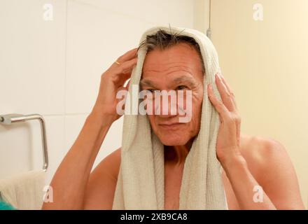 Homme mûr séchant son visage dans la salle de bain avec une serviette après la douche Banque D'Images