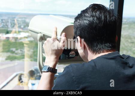 Jeune homme regardant à travers un Visualiseur de tour à monnaie ou des jumelles stationnaires un sommet d'un bâtiment Banque D'Images