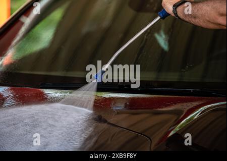 Lavage de voiture manuel avec de l'eau sous pression dans le lavage de voiture à l'extérieur. Lavage de voiture d'été. Banque D'Images