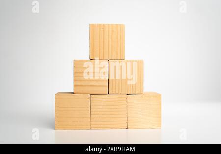 Les blocs de cube en bois vierges vides construisent une forme pyramidale avec le grand sur le dessus, isolé sur le bureau en bois sur fond blanc. Processus de croissance de l'entreprise, educat Banque D'Images