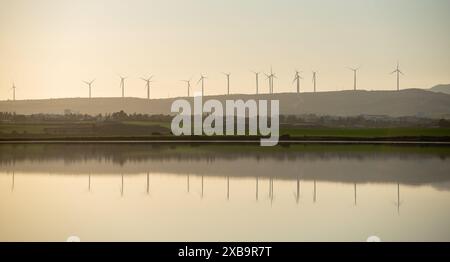 Vue sur le lac au coucher du soleil. Parc de centrales éoliennes pour les énergies renouvelables au bord des montagnes Banque D'Images