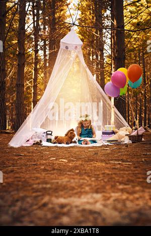 Pique-nique, fille et livre de lecture dans les bois pour le développement, l'éducation ou l'histoire de conte de fées. Nature, fantaisie et jeune enfant sur couverture avec costume pour Banque D'Images