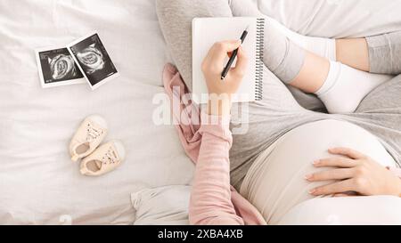 Vue ci-dessus de la femme enceinte écrivant dans le cahier dans le lit Banque D'Images