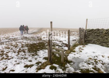 Un stile sur Branstree entouré de neige de fin d'automne avec un groupe de marcheurs au loin. Mardale, parc national de Lake District, Cumbria, Angleterre. Banque D'Images