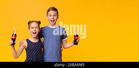 Heureux enfants buvant Coca-Cola Classic avec des pailles sur orange Banque D'Images