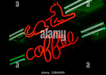 Une enseigne au néon affichant le mot « café » avec un design stylisé de chat dans des couleurs vives rouge et vert. Banque D'Images