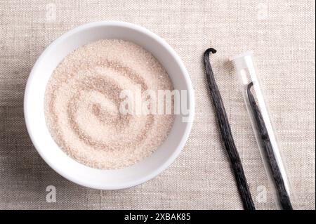 Sucre vanillé, sucre aromatisé dans un bol blanc sur tissu de lin, à côté de gousses séchées, brunes, mûres ou haricots de Vanilla planifolia, une épice. Banque D'Images