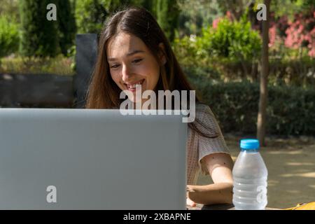 Étudiante souriante et interagissant avec son ordinateur portable sur le campus. Vie étudiante, technologie, éducation, début des classes. Banque D'Images