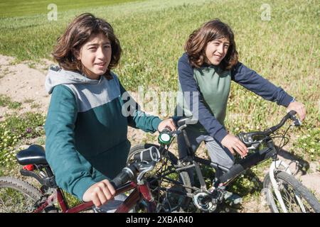 Frères jumeaux adolescents sur un vélo dans un pré posant en regardant la caméra. Activités de plein air. Banque D'Images