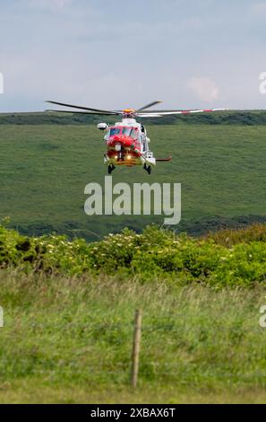 L'hélicoptère de recherche et de sauvetage de garde côtière se prépare à atterrir sur le sommet de la falaise Un sauvetage spectaculaire impliquant le service d'ambulance aérienne, les garde-côtes, RNLI Banque D'Images