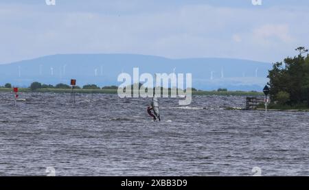 South Shore Lough Neagh, County Armagh, Irlande du Nord, Royaume-Uni. 11 juin 2024. Météo britannique - près de la mi-juin et une autre journée froide pour la période de l'année dans le flux d'air nord. Ciel gris avec l'éclatement occasionnel de la lumière du soleil a vu des températures autour de 12C aujourd'hui. Un windsurfeur profite au maximum des conditions sur le Lough Neagh. Crédit : CAZIMB/Alamy Live News. Banque D'Images