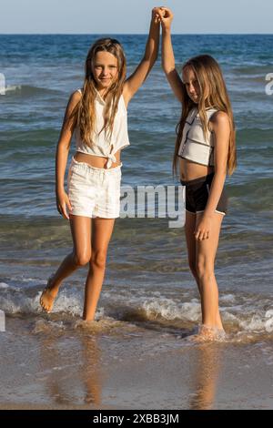 Cette image capture magnifiquement l'harmonie joyeuse de deux belles soeurs jumelles aux longs cheveux blonds et aux yeux verts, profitant d'une promenade sereine sur le b. Banque D'Images