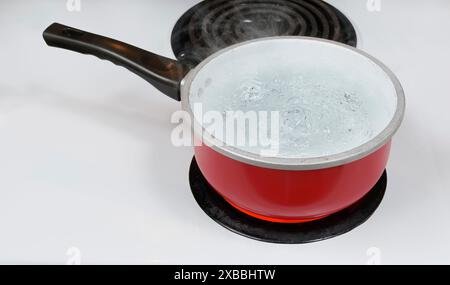 Plan horizontal regardant vers le bas sur une casserole rouge d'eau bouillante sur un brûleur supérieur de cuisinière électrique. Banque D'Images