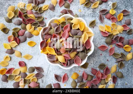 Fond de pâtes coloré. Vue de dessus des coquilles de pâtes cinq couleurs sur fond de pierre blanche. Pâtes au curcuma, aux épinards, à la betterave et à la carotte noire. Banque D'Images