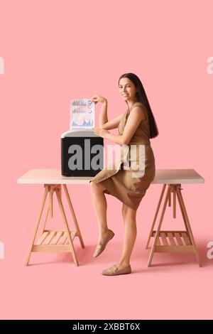 Jeune femme détruisant des documents à l'aide d'un déchiqueteur sur la table sur fond rose Banque D'Images