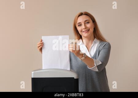 Femme adulte détruisant la feuille de papier à l'aide d'un déchiqueteur sur fond clair Banque D'Images