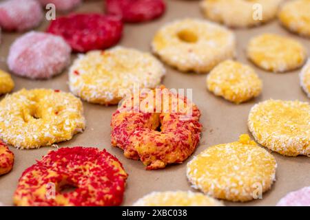 Gros plan de biscuits jaunes et rouges, prêts à cuire, dans des flocons de noix de coco sur une plaque à pâtisserie. Banque D'Images