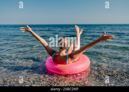 Une femme flotte dans un radeau gonflable rose sur une plage. Elle sourit et elle s'amuse Banque D'Images