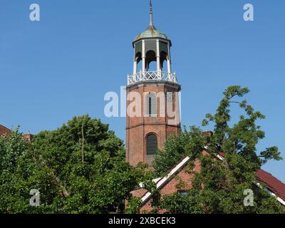 Tour historique de l'église s'élève au-dessus des arbres et des bâtiments, sous un ciel bleu clair, Ditzum, rheiderland, basse-Saxe, Allemagne Banque D'Images