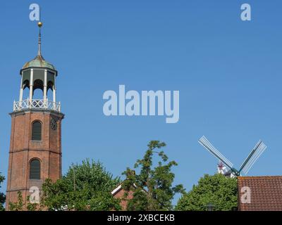 Tour d'église et moulin à vent, entouré d'arbres verts et ciel bleu dans un paysage d'été, Ditzum, rhénanie, basse-Saxe, Allemagne Banque D'Images