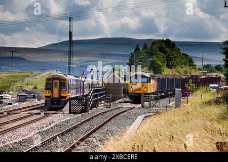 Locomotive Northern Rail classe 158 et Colas Rail Freight classe 56 avec un train de marchandises transportant du bois à la gare de Ribblehead, Yporkshire, Royaume-Uni Banque D'Images