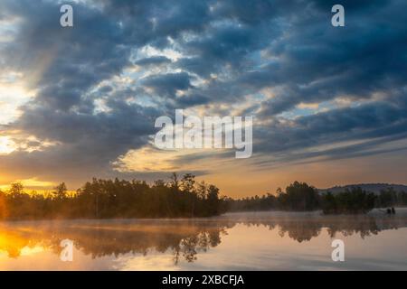 Brouillard sur le lac au lever du soleil, nuages spectaculaires et reflétant la surface de l'eau dans un environnement naturel, dans la lande Banque D'Images