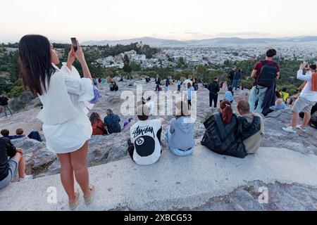 Touristes assis sur le rocher Areopagus au coucher du soleil, femme prenant des photos du panorama de la ville avec son téléphone portable, Athènes, Grèce Banque D'Images