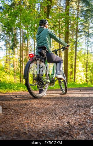 Une personne fait du vélo sur un chemin forestier entouré de grands arbres dans une forêt verdoyante, E-Bike, Forêt Noire, Gechingen, Allemagne Banque D'Images