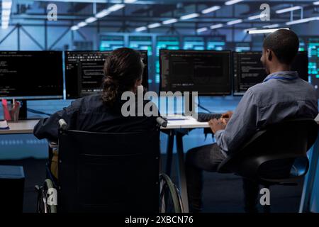 Personne paraplégique et collègue travaillant dans un espace de travail de hub de serveur inclusif, tapant sur PC. Femme en fauteuil roulant et collègue effectuant des tâches dans le centre de données abritant une infrastructure de stockage de données avancée Banque D'Images