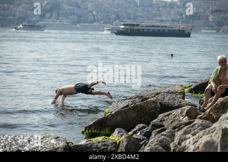 Un homme saute des rochers dans la mer. Alors que le temps chaud a fait effet à Istanbul, les thermomètres ont atteint 33 degrés Celsius. Des gens ont été vus nager dans la mer pour se rafraîchir sur la plage d'Uskudar Salacak. Banque D'Images