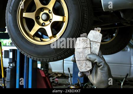 Concept d'entretien du système de freinage de voiture , main de mécanicien tenant une plaquette de frein de voiture dans le garage de réparation de voiture Banque D'Images