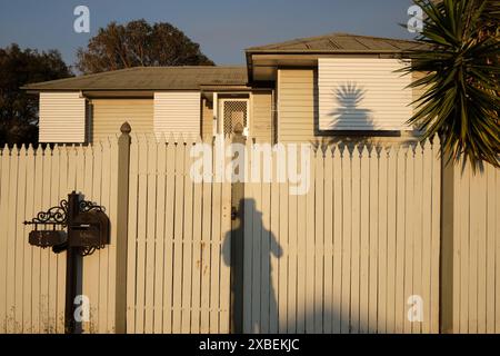 Shadow selfie contre une clôture de piquet devant une maison de banlieue soignée avec une boîte aux lettres élaborée lors d'une journée ensoleillée à Carina, Brisbane Banque D'Images