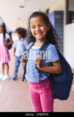 Fille biraciale souriante avec sac à dos, prête pour l'école Banque D'Images