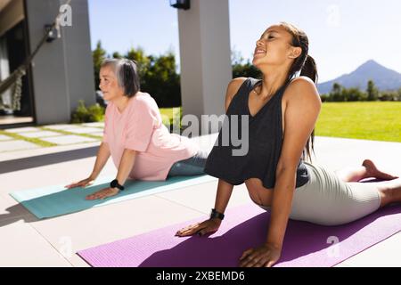 Grand-mère asiatique et petite-fille biraciale pratiquant le yoga sur des tapis à l'extérieur Banque D'Images