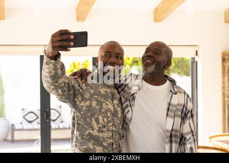 Jeune soldat afro-américain en uniforme militaire prenant selfie avec son père mûr. Ils sont à l'intérieur avec de grandes fenêtres et streami de lumière naturelle Banque D'Images