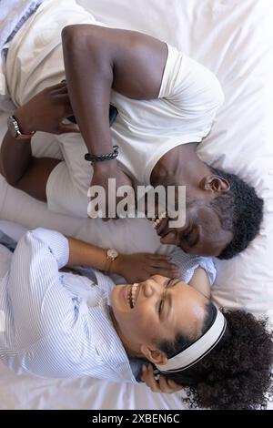 Un couple diversifié est allongé sur le lit, riant et profitant de la compagnie de l'autre Banque D'Images