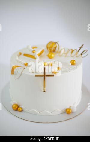 Un élégant gâteau blanc avec des décorations dorées et une croix, parfait pour les célébrations religieuses. Banque D'Images